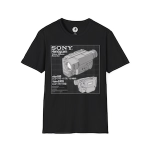 May include: Black t-shirt featuring a graphic of a Sony Handycam video camera. The design includes the text "SONY Handycam Video Camera Recorder" and model details. The graphic is in shades of gray and white.