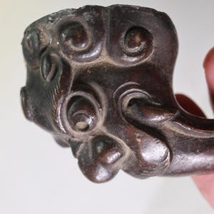 May include: Close-up of a dark brown, intricately carved wooden pipe bowl. The bowl features detailed swirling patterns and a curved stem, showcasing a vintage aesthetic. The wood has a rich, aged appearance.