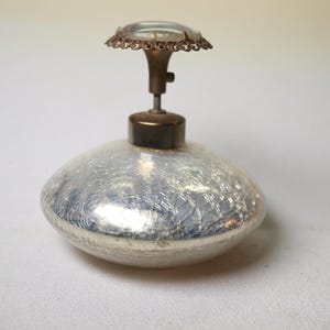 May include: A vintage perfume bottle with a silver crackle glass body and a decorative top. The top features a small, clear glass dome surrounded by a delicate metal filigree. The bottle has a classic, elegant design.