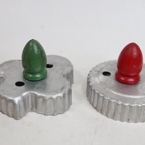 May include: Two metal cookie cutters with wooden handles. One cutter is clover-shaped with a green handle, and the other is circular with a fluted edge and a red handle. Both cutters feature small circular holes in the metal base.