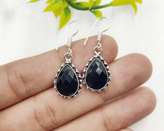 May include: A pair of silver-toned drop earrings with teardrop-shaped black gemstones. The earrings have a textured border and a simple hook closure. The gemstones are faceted, catching the light and adding a touch of elegance.