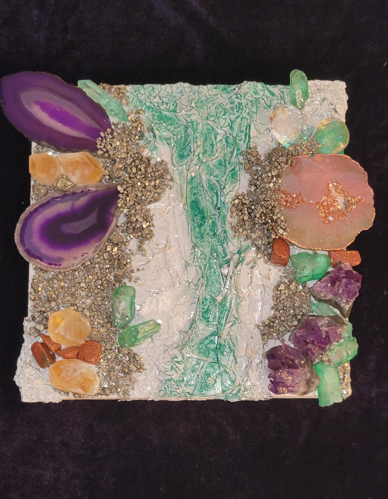May include: A mixed media art piece featuring a variety of crystals and stones, including amethyst, agate, and pyrite. The piece is set on a white background with a green and white textured surface.