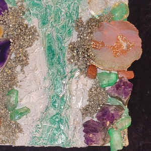 May include: A mixed media art piece with a white background and various textures. The piece features green, purple, and pink crystals, as well as gold and brown accents.