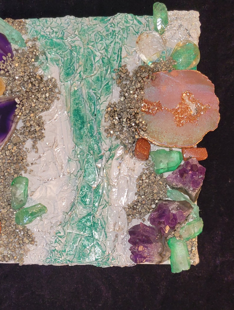 May include: A mixed media art piece with a white background and various textures. The piece features green, purple, and pink crystals, as well as gold and brown accents.