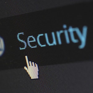 May include: Close-up of a computer screen displaying the word "Security" in light blue. A white hand cursor points towards the word. A small icon is visible to the left of the word. The background is dark.
