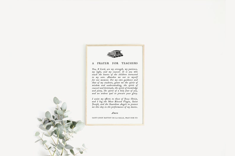 May include: Framed print with the text "A Prayer for Teachers" in black font. The print has a beige border and is set against a white background. A sprig of green leaves is in the lower left corner.