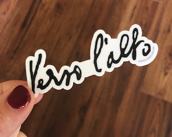 Op de afbeelding: Witte sticker met zwarte cursieve tekst die "Vero l'alfa" luidt, met een websiteadres in kleiner lettertype in de rechterbenedenhoek.