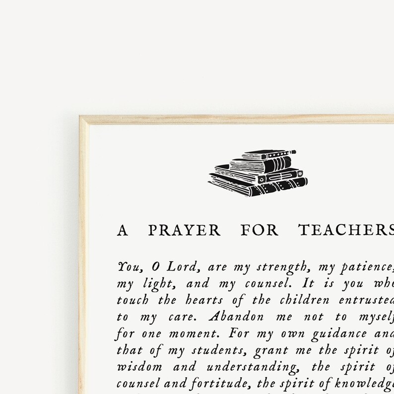 May include: A framed print with the text "A Prayer for Teachers" in black font. The print features a stack of books at the top. The background is a light cream color, and the frame is a light wood color.