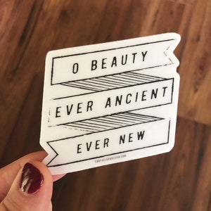 May include: White sticker with black text that reads "O Beauty Ever Ancient Ever New" with a website address at the bottom. The sticker is in the shape of a banner.