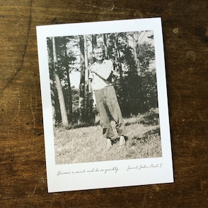 May include: A black and white photo of a man smiling in a forest. The photo has the quote "Become a saint, and do so quickly. - Saint John Paul II" written at the bottom.