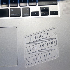 May include: A white sticker with black text on a silver laptop. The text reads "O Beauty Ever Ancient Ever New".