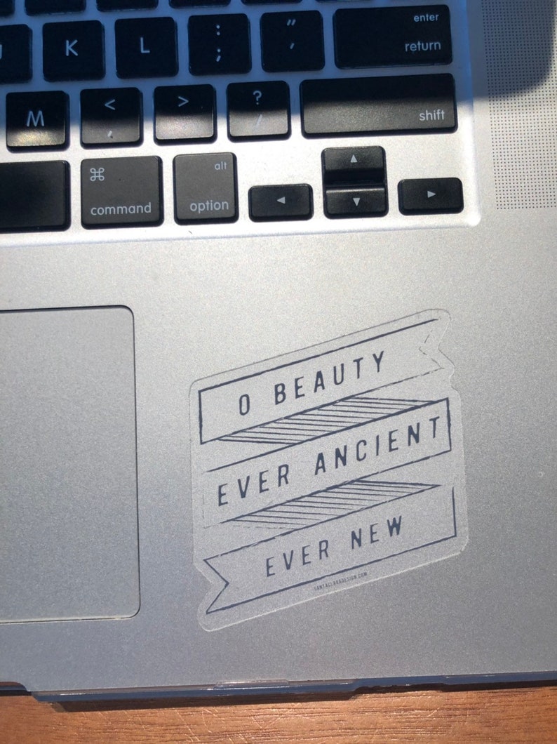 May include: A white sticker with black text on a silver laptop. The text reads "O Beauty Ever Ancient Ever New".