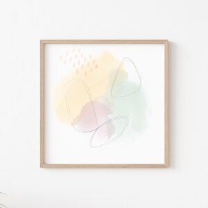 Op de afbeelding: Abstracte kunstprint met een gele, groene en paarse aquarel achtergrond en dunne zwarte lijnen. De print is ingelijst in een licht houten frame.
