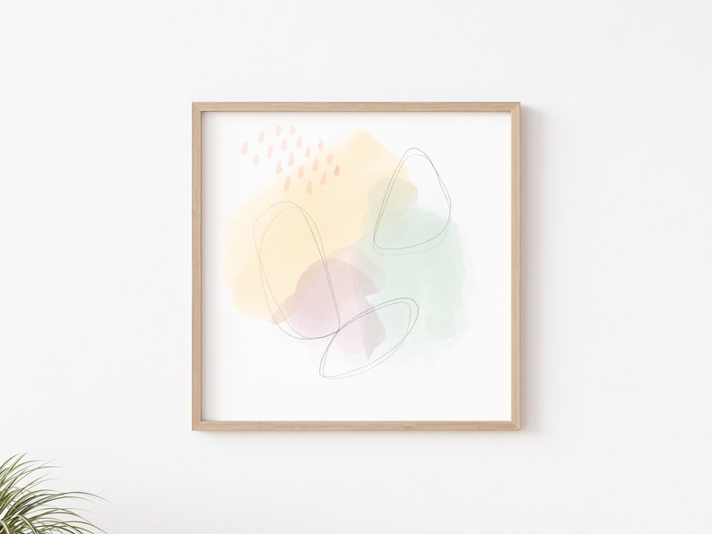 Op de afbeelding: Abstracte kunstprint met een gele, groene en paarse aquarel achtergrond en dunne zwarte lijnen. De print is ingelijst in een licht houten frame.