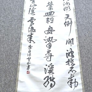 May include: A traditional Japanese scroll featuring black calligraphy on white paper. The scroll has a decorative border and a wooden dowel at the bottom. The calligraphy is in vertical columns and includes a red seal.