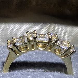 May include: A gold ring with five rectangular diamonds set in a row. The ring's band is gold, and the diamonds sparkle. This ring is likely a piece of fine jewellery.