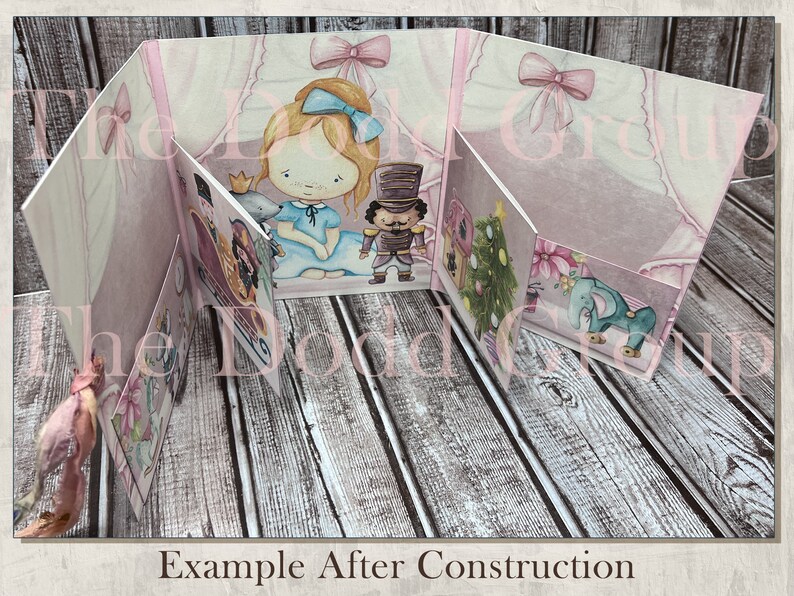 May include: A pink and white papercraft pop-up card with a girl, a nutcracker, a Christmas tree, and an elephant. The card is open and the pop-up elements are visible. The card is on a wooden surface.  Example After Construction