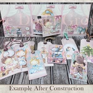 May include: A set of 10 Christmas-themed gift tags featuring illustrations of a nutcracker, a mouse, a clock, a girl in a blue dress, a girl in a white dress, a girl in a pink dress, a church, a snowman, a Christmas tree, and a rocking horse. The tags are printed on a textured paper with a pink and white background.
