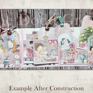 May include: A set of eight pink and white Christmas-themed gift tags with various illustrations, including a ballerina, a nutcracker, a rocking horse, a snow globe, and a Christmas tree. The tags are decorated with glitter and have a rustic wood background.
