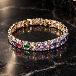 Könnte beinhalten: Ein goldfarbenes Armband mit zwei parallelen Reihen aus baguettegeschliffenen Steinen in verschiedenen Farben wie Rot, Grün, Gelb, Violett, Blau und Transparent. Die Metallglieder sind in einem Muster mit einem Verschluss verbunden.