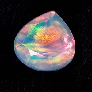 Può includere: Una gemma iridescente a forma di pera con un arcobaleno di colori, tra cui rosa, giallo, verde e blu. La gemma ha una superficie sfaccettata ed è posta su uno sfondo nero. La gemma è probabilmente un'opale.
