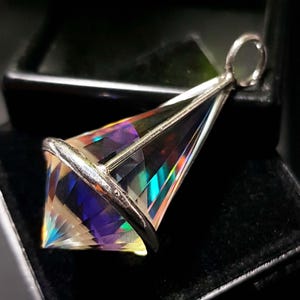 May include: A prism-cut pendant with a silver-colored metal setting. The pendant is a clear crystal with iridescent rainbow colors. The pendant is in a triangular shape with a loop at the top.