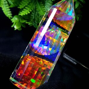 Puede incluir: Una punta de cristal prismática con una superficie pulida y facetada. El cristal muestra un espectro de colores, incluyendo azules, naranjas y verdes, con una calidad clara y reflectante. El cristal mide unos 15 cm de largo.