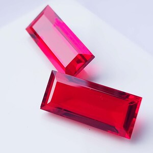 Può includere: Due gemme rettangolari sfaccettate in tonalità di rosso. Le gemme hanno un aspetto lucido e trasparente, con bordi affilati e un colore vibrante. Le gemme sono probabilmente per la creazione di gioielli o la collezione.