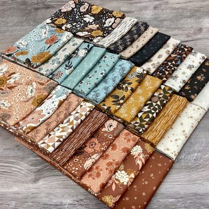 May include: A collection of folded fabric squares arranged in a grid, featuring a variety of patterns including floral prints, geometric shapes, and abstract dots in a color palette of brown, tan, cream, blue, black, and mustard yellow.