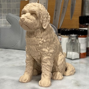 May include: A beige-colored dog figurine in a sitting position. The sculpture has detailed fur texture and is positioned on a marble surface. The background includes kitchen utensils and spice jars.