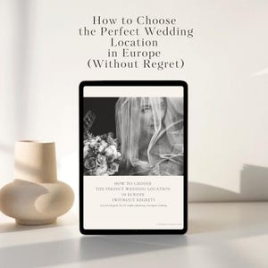 Op de afbeelding: Een digitale tablet toont een huwelijksgids met de titel "How to Choose the Perfect Wedding Location in Europe (Without Regret)". De afbeelding op de tablet toont een bruid met een boeket. Links staat een beige vaas.