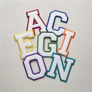 May include: A collection of seven varsity-style letter patches arranged in a cluster. The letters A, C, E, G, I, O, and N are white with thick, colorful embroidered borders in red, blue, yellow, green, orange, purple, and teal respectively.