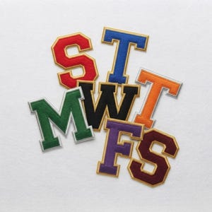 May include: A collection of seven embroidered varsity-style letter patches in various colors, including red, blue, green, black, orange, purple, and maroon. Each letter features a bold block font with a contrasting border, arranged in a cluster.
