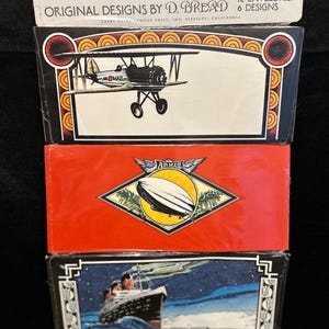 May include: A stack of vintage "Envelope Art" boxes featuring original designs. The top box displays a biplane, the middle box showcases an airship, and the bottom box depicts a ship. Each box contains 12 envelopes with 6 designs.