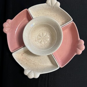 May include: A ceramic serving set with a central round bowl and four surrounding fan-shaped dishes. The dishes are pink and speckled beige, with a decorative scalloped edge. The central bowl is beige with a starburst design.