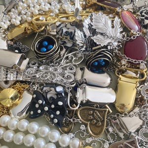 May include: A collection of vintage jewelry pieces, including brooches, necklaces, and clips. The assortment features silver, gold, and pearl accents, with various designs such as leaves, bows, and hearts. Some pieces have embedded gemstones and enamel details.