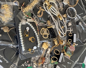 May include: A collection of various jewelry pieces, including necklaces, bracelets, earrings, and rings. The jewelry features gold and silver tones, with pearls, gemstones, and decorative elements. Some pieces are packaged on black cards.
