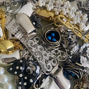 May include: A collection of vintage jewelry pieces, including brooches, necklaces, and earrings. The assortment features silver, gold, and pearl accents, with some pieces adorned with rhinestones and enamel details. A black and white bow-shaped brooch is also visible.