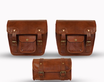 May include: Three brown leather saddlebags with brass-colored hardware. Two larger bags have a flap with a buckle closure and a front pocket. The smaller bag has two buckle closures and two straps. All bags are made of brown leather.