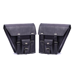 May include: Two black leather motorcycle saddlebags with multiple pockets and silver buckles. Each bag has a triangular shape and a flap closure. The bags are designed to be mounted on the sides of a motorcycle.