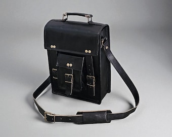 May include: Black leather satchel with a top handle and adjustable shoulder strap. The bag has a front flap pocket with buckle closures and brass-coloured hardware. A classic, structured design.