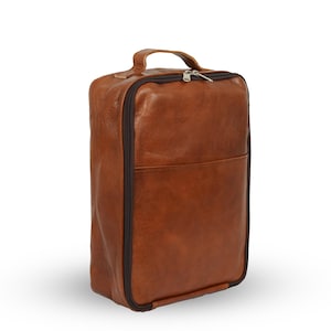 Puede incluir: Una bolsa de zapatos rectangular de cuero marrón con un asa superior y una cremallera envolvente. La bolsa tiene un pequeño bolsillo frontal y una cremallera y ribete marrón oscuro.