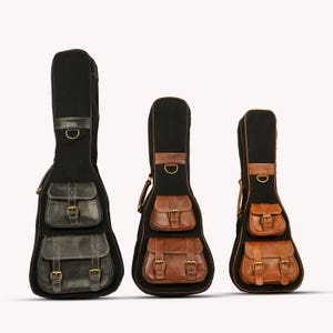 Peut inclure: Trois étuis de guitare de tailles différentes. Les étuis sont noirs avec des détails et des poches en cuir marron. Chaque étui comporte deux poches avant avec des boucles et une poignée en cuir. Conçu pour protéger et transporter les guitares.