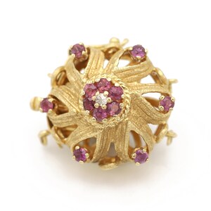 May include: A gold pendant with a delicate, intricate design featuring a central cluster of pink gemstones surrounded by smaller pink gemstones. The pendant has a starburst shape and is suspended from a gold chain.