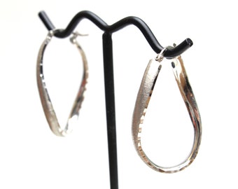 May include: A pair of silver hoop earrings with a textured finish. The earrings are hanging on a black display stand.