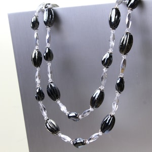 May include: A double strand necklace with black and clear oval beads. The necklace is made of glass beads and is approximately 20 inches long.