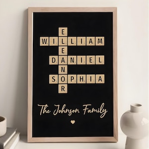 May include: Framed black artwork featuring a crossword puzzle design with names spelled out in wooden letter tiles. The names are William, Daniel, and Sophia. The text "The Johnson Family" is written below the crossword, with a heart symbol. The frame is light brown.