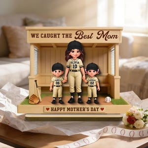 May include: A baseball-themed figurine featuring a mother and two children in baseball uniforms. The figurine is set in a wooden dugout with the text "WE CAUGHT THE Best Mom" and "HAPPY MOTHER'S DAY". A baseball, glove, and bat are also included.