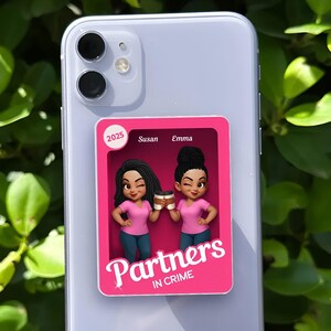 May include: A pink phone grip featuring two cartoon women holding coffee cups. The text "Partners in Crime" is displayed below the women. The names "Susan" and "Emma" are above the women, and the number "2025" is in a circle.