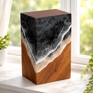 May include: A wooden block with a dark brown top and a lower section of natural wood grain. The middle section features a black and white resin design resembling ocean waves. The piece is displayed on a white windowsill.